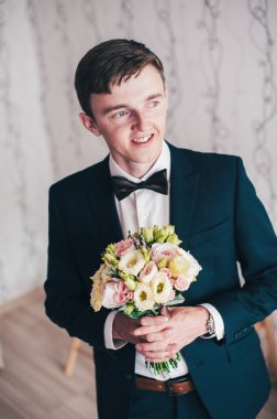 Mutlu damat ayakta duruyor ve poz veriyor. Düğün sabahı. Kapat. Geçmişi. Gülümse, portre. Elinde bir buket gül..