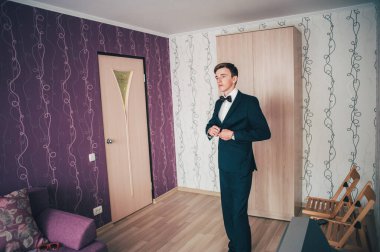 Damat ayakta, şık bir odada ceket giyiyor. Mutlu damat pozu. Düğün sabahı. Geçmişi. Gülümse, portre.