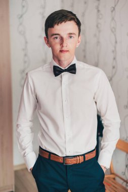 Ayakta duran ve poz veren mutlu damat. Düğün sabahı. Yaklaştın. Arka planda şık odalar, daireler var..