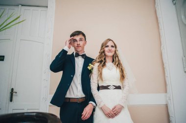 Zarif, zarif bir gelin ve damat arka planda, beyaz kapılar ardında dururlar. Katlanmış eller. Kapatın. Portre. Geçmişe dönüş. Kapalı alanda klasik mimari. Mutlu ve gülümseyen yeni evliler.