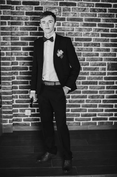 一个华丽而优雅的新郎带着眼镜站着 在婚礼上摆姿势 在砖墙的后面 靠近点黑白照片 肖像画 — 图库照片
