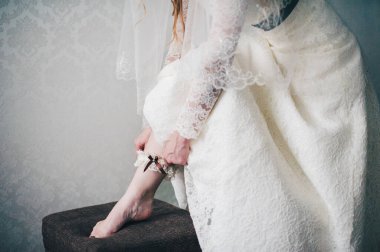 El, bacağına sargı bezi takıyor. Yakın plan. Günaydın Gelin. Düğün günü. Şık bir elbise. Mimonette. Kapat. Yarı elbise. Beyaz duvar dairesinin arka planına karşı..