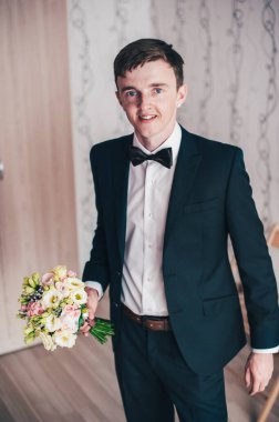 Mutlu damat ayakta duruyor ve poz veriyor. Düğün sabahı. Kapat. Geçmişi. Gülümse, portre. Bir buket gül.