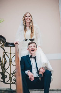 Zarif, zarif bir gelin damadın üzerine basar merdivenlere çıkar, parmaklıklar ve desenlerle. Kapatın. Portre. Geçmişe dönüş. Kapalı alanda klasik mimari. Sahte metal merdiven