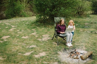 Doğada ateşe yakın dizüstü bilgisayardan aileyle iletişim. Evde eğitim, serbest meslek. Anne, çocuklarla internette çalışıyor. Karantina, Coronavirüs salgını sırasında kapalı anaokulu..