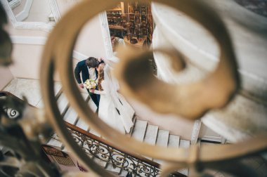 Zarif, zarif bir gelin ve damat merdivenlerde aynanın yanında durmuş desenlerle sarmaş dolaş öpüşüyor. El ele tutuşun Sarılalım. Kapatın. Portre. Geçmişe dönüş. Kapalı alanda klasik mimari. Sahte metal merdiven