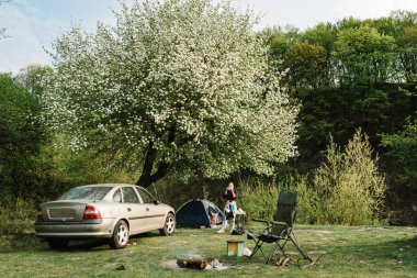 Ateşin yanında piknikte kahve içen bir kız. Dinlen ve doğada çadırlarla tatil yap. Seyahat konsepti. Mutlu aile tatilleri..