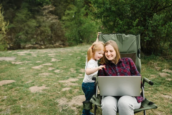 Communication with family online on laptop near fire in nature. Homeschooling, freelance job. Mother work on Internet with kid outdoors. Quarantine, closed nursery school during coronavirus outbreak.
