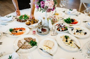 Garson şenlik masasında yemek servisi yapar. Yemek, salata, et, balık menüsü. Düğün ziyafetinde şölen masası. Sanat eserleri. Dekorasyon. Ayrıntılar.