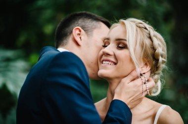 Yeşilliğin arka planında duran ve öpüşen damat ve gelinin portresi. Botanik yeşil bahçesinde düğün töreni.