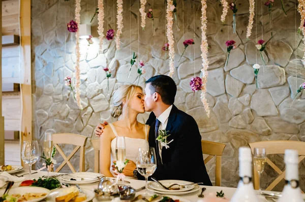 연회장에서 신부와 신부가 식탁에서 키스를 실내의 부부들 입니다 과푸른 초목으로 — 스톡 사진