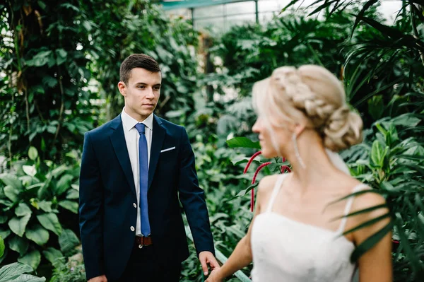 結婚式のスーツを着た新郎とドレスの花嫁の肖像画は緑豊かな植物園で起こっています 結婚式だ 新婚旅行だ — ストック写真