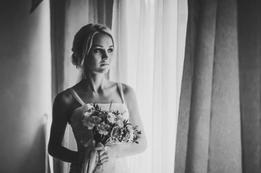 Bir buket çiçekli şık gelin odalardaki pencerenin yanında. Siyah beyaz fotoğraf.