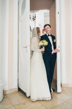 Bir buket çiçekli şık bir gelin damada sarılıyor, ayağa kalkıyor, bakıyor ve kapıyı açıyor. Kapatın. Portre. Geçmişe dönüş. Kapalı alanda klasik mimari. Kapıdan çık..