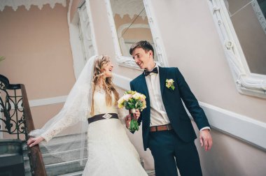 Zarif, zarif bir gelin ve damat merdivenlerde aynanın yanına gider. Buketi elinde tutuyor. Sarılalım. Kapatın. Portre. Geçmişe dönüş. Kapalı alanda klasik mimari. Sahte metal merdiven