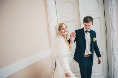 Şık, zarif bir gelin damat ile dans ediyor ve kapının yanında el ele tutuşuyor. Kapatın. Portre. Geçmişe dönüş. Klasik mimari içeride..