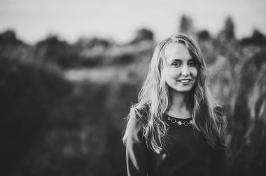 Sonbaharda kırmızı elbiseli güzel bir kızın portresi doğanın arka planında duruyor. Üst yarısı. Önüne bak. Kapatın. Siyah beyaz fotoğraf.