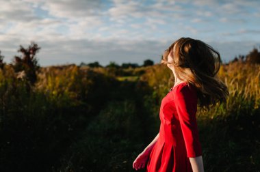 Güzel bir kızın portresi, sonbaharda kırmızı bir elbiseyle doğanın arka planına yaslanır. Üst yarısı. Kapatın. Rüzgârın savurduğu saçlar.