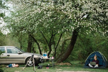 Kampta internette çocukla birlikte çalışan bir anne. Koronavirüs salgını sırasında karantina ve kapalı anaokulu. Serbest bir iş. Araba ve çadırın yanında bir çocukla aile tatili..