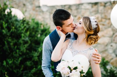 Şık, mutlu bir gelin, tacı ve damadı olan bir kadın, dostum. Yeni evliler sarılıp öpüşüyorlar. Kapatın. Doğanın arka planında. Bir erkek bir kadına arkadan sarılır ve dudaklarını öper..