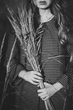 Elinde bir buket kurumuş çimen, arka planda uzun bir çimen ve sonbaharda doğada saçlar. Ortalama yarım boy. Kapatın. Siyah beyaz fotoğraf.