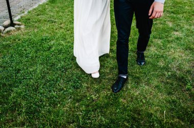 Damadın bacakları çimlerin üzerinde. Gelin ve damat. Yeni evliler. Gelinliğin bir parçası ve erkek pantolonu..