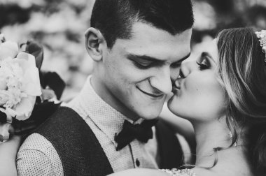 Bir buket şakayık çiçekli şık mutlu gelin, damadı öpüyor. Yeni evliler. Kapatın. Düğün, nişan, evlilik teklifi, flört. Siyah beyaz fotoğraf