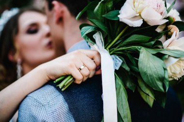 Arka planda düğün buketi, bir buket şakayık öpücüklü şık mutlu gelin damat. Yeni evliler. Kapatın. Düğün, nişan, evlilik teklifi, çıkma..