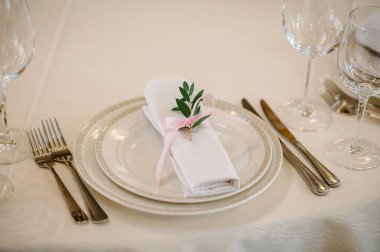 Servis, kurma masası. İki tabak, cam bardak, keten peçeteli çatal bıçak takımı pembe kurdeleli, dal yeşili. Düğün masası dekorasyonu. Sanat eserleri. Kapatın. Yan görünüm.