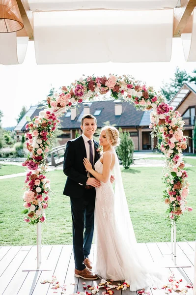 裏庭の宴会エリアで花や緑で飾られたアーチの下で結婚式の後に立って幸せな花嫁と新郎 新婚夫婦で — ストック写真