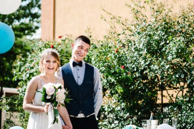 Bir buket şakayık ve damat elele tutuşmuş şık mutlu gelin. Balonların arka planında evin avlusundaki doğada. Töreni bekliyorum. Düğün sabahı. Kapat..