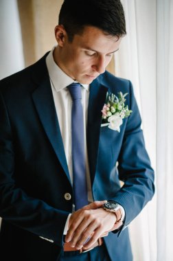 Bir adam kolundaki saati ayarlar. Saat kullanarak iş adamına yaklaş. Gelinlik giymiş mutlu bir portre. Odaların penceresinin yanında duran yaka çiçekli..