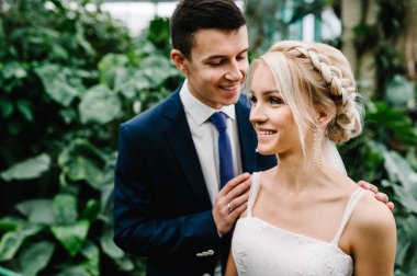 Damat ve gelinlik giymiş gelinin portresi botanik bahçesinde yeşillik içinde duruyor ve sarılıyorlar. Düğün töreni..