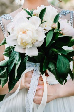 Şık, görkemli, şakayık gelin buketi. Kapatın. Gelinin arka planında. Gelinin elinde bir buket pembe çiçek tutarken görüntüsü. Güzel bir buket. Dantel, yay, kurdele.