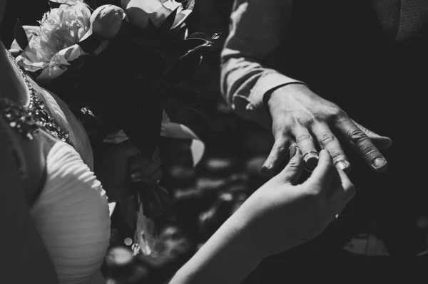 牡丹の花束を持つスタイリッシュな花嫁は 新郎の指の手に金の指輪を身に着けています 自然を背景に 結婚式だ 閉めろ 白黒写真 — ストック写真