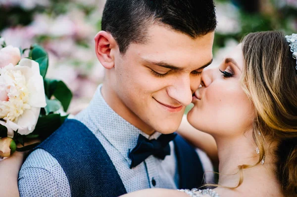 Bir buket şakayık çiçekli şık mutlu gelin, damadı öpüyor. Yeni evliler. Kapatın. Düğün, nişan, evlilik teklifi, çıkma..