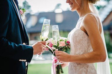 Gelin ve damat bir buketle ellerinde şampanya kadehleriyle kemerin altında çiçek ve bahçedeki ziyafet alanının yeşilliği ile süslenmiş bir şekilde duruyorlar..
