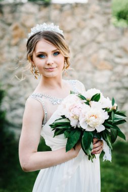 Bir buket şakayık desenli, arka bahçede poz vermiş neşeli bir gelin. Kapatın. Doğa. Taş duvarın arka planına karşı. İleriye, ileriye..