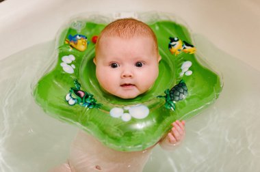 Bebek yeni doğdu, kız banyoda boynunda şişirilebilir bir halkayla banyo yapıyor..