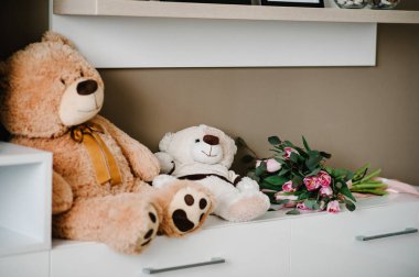 İki pelüş peluş oyuncak ayı ve bir buket çiçek beyaz arka planda, odada yatıyor. Mutlu bir gün, bir tatil hediyesi..