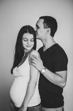 Hamile bir eşin elleri gibi ayakta duran ve karnını tutan bir koca resmi. Kadın, kız ve erkek evde öpüşüp göbeğe sarılıyorlar. Sevgi dolu çift. Ebeveynlik kavramı. Bebek partisi. Siyah-beyaz Aile fotoğrafı.