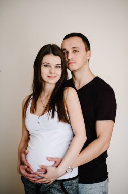 Hamile bir eşin elleri gibi ayakta duran ve karnını tutan bir koca resmi. Kadın, kız ve sevgi dolu yakışıklı adam evde karnına sarılıyor. Sevgi dolu çift. Ebeveynlik kavramı. Bebek partisi. Aile fotoğrafı..