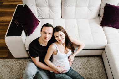 Kocanın hamile bir kadının elleriyle oturup karnını tuttuğunu hayal et. Kadın, kız ve erkek evde göbeğe sarılıyor. Sevgi dolu çift. Ebeveynlik kavramı. Bebek partisi. Aile fotoğrafı..