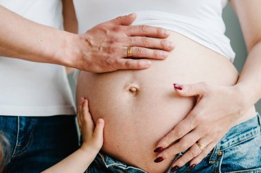 Kocasının kesilmiş görüntüsü, hamile karısının karnını tutan kızı sembolik eller yapıyor. Hamile kadın ve sevgi dolu yakışıklı adam evde karnına sarılıyor. Sevgi dolu çift. Ebeveynlik kavramı. Bebek Duşu.