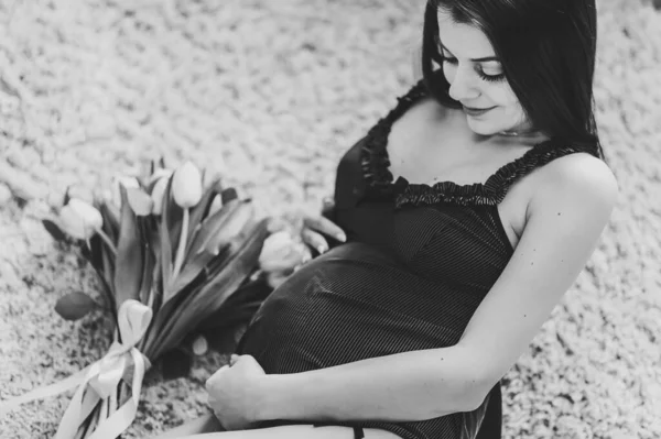 怀孕的性感女人躺在地板上或床上 抱着一束鲜花摸着肚子 抱着肚子回家 母亲的概念 黑白照片 — 图库照片