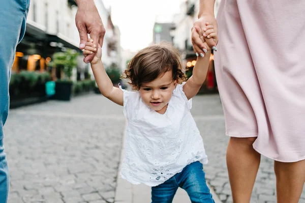 Anne, baba küçük kızı tutuyor. Genç mutlu aile: baba, kız, anne eski şehrin, kasabanın, açık havanın antik mimarisinin yakınında sokaklarda yürüyor. Aile tatili ve seyahat kavramı.