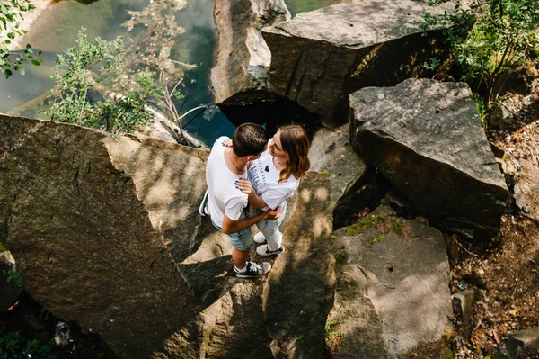 若いカップルは湖の近くに石を抱いている 岩を背景に男と女が立っている 最上階だ お互いを見ていると — ストック写真