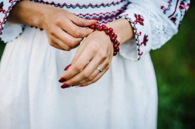 Tırnaklarında kırmızı bir leke olan kadın eli manzarası ve kırsal stilde sonbaharda değerli taşlar takan güzel bir bilezik. Ukrayna tarzı: doğada nakışlı giysiler içinde gelin.