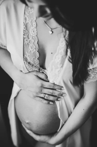 怀孕妇女手牵着肚子 女孩抱着一个圆圆的肚子靠近窗户在家里 产妇概念 靠近点9个月 小宝宝洗澡 前面的景色 黑白照片 — 图库照片