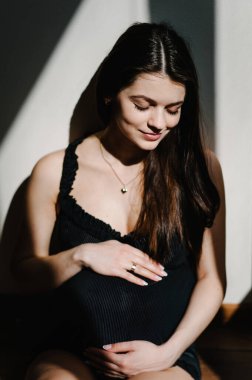 Bekliyorum bebeğim. Hamile bir kadın oturur ve elleri karnını ve karnını sarar. Yakın plan. Dokuz ay. Bebek partisi. Annelik kavramı. ön görünüm.